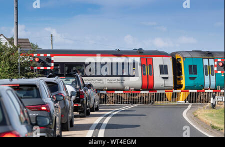 Cars queuing up at a level crossing as a train passes. Wales, UK.