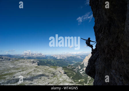 Horizontal view of an attractive blonde female climber in silhouette on a steep Via Ferrata pointing to the sky Stock Photo