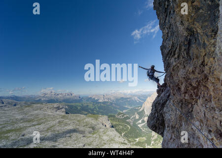 Horizontal view of an attractive blonde female climber on a steep Via Ferrata pointing to the sky Stock Photo