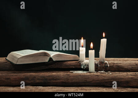 Beautiful open bible and burned candles on a old oak wooden table. Background of  smoke. Stock Photo
