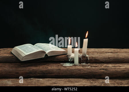 Beautiful open bible and burned candles on a old oak wooden table. Background of  smoke. Stock Photo
