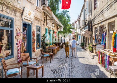 Alacati, Turkey - September 4th 2019: Couple walking down a narrow street with shops. The town is a popular tourist destination, Stock Photo