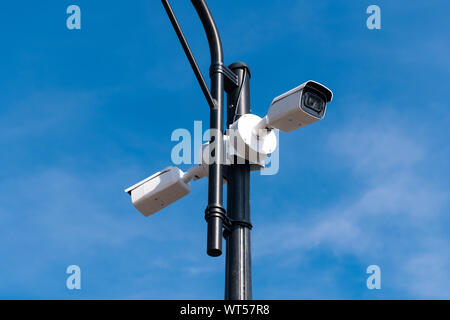 Two white surveillance cameras on the metal lamp post against blue sky. Security of the whole territory. Security service is watching. Copy space. Stock Photo