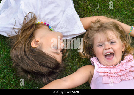 Two little girls laying on the grass, laughing and having fun Stock Photo