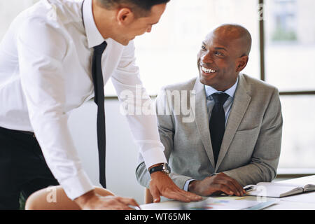 Laughing African American businessmen discussing paperwork with a coworker at a table in an office Stock Photo