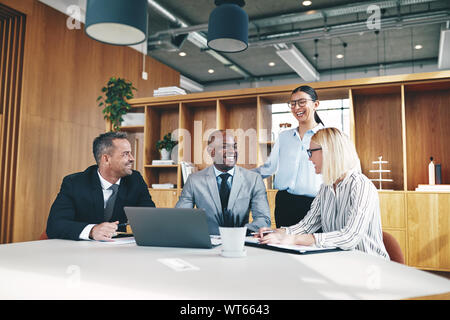 Diverse group of businesspeople talking and laughing together while working around a talbe in an office Stock Photo