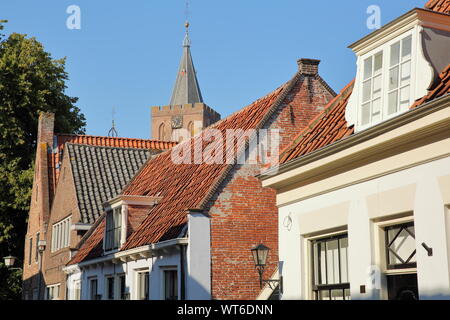 Historic houses located inside the fortified town of Naarden, Netherlands, with the clock tower of the Grote Kerk church in the background Stock Photo