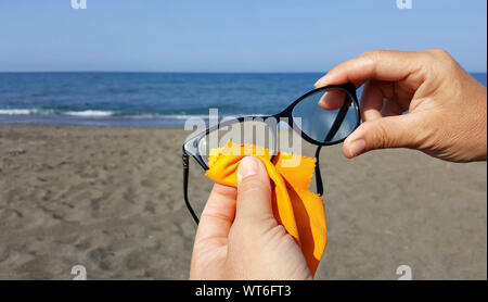 Closeup of hands cleaning glasses lens with orange cloth lens on the beach Stock Photo