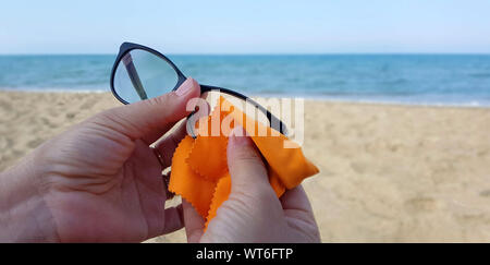 Closeup of hands cleaning glasses lens with orange cloth lens on the beach Stock Photo