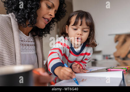 Caring mother and her adorable little girl coloring at home Stock Photo