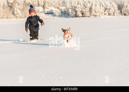 Happy kid playing with dog in deep snow at sunny winter day Stock Photo