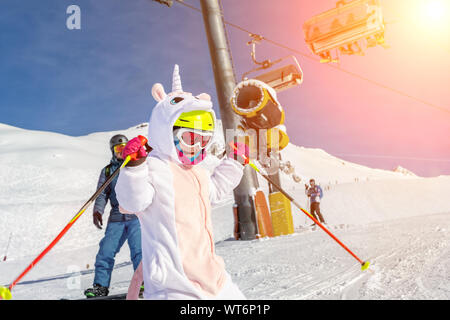 Cute adorable preschooler caucasian kid girl portrait with ski in helmet, goggles and unicorn fun costume enjoy winter sport activities. Little child Stock Photo