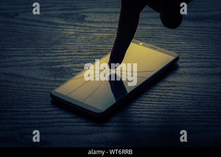 close up of a human finger touching a cracked phone screen - Cyber bullying concept Stock Photo