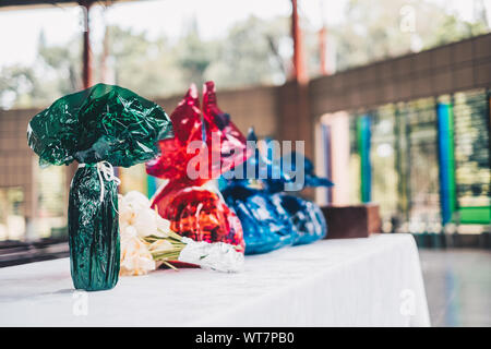 Food and other grocery items wrapped in green, red, and blue water cellophanes and flower ready on the table for offertory during Eucharist Stock Photo