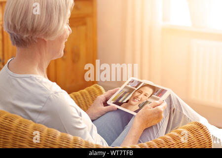 technology and senior people concept, elderly woman with tablet pc viewing family photo album at home Stock Photo