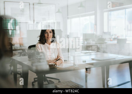 Smiling young businesswoman sitting inside of her office Stock Photo