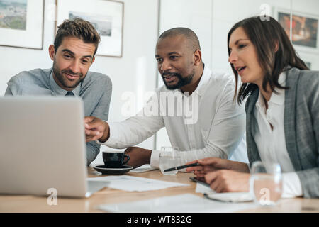 Smiling businesspeople working with a laptop during an office meeting Stock Photo