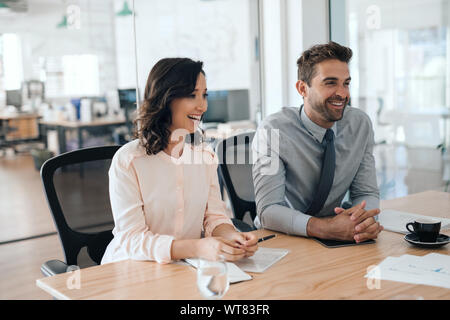 Two laughing businesspeople sitting together in an office boardroom Stock Photo