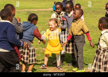 Imani Junior Academy, Nanyuki, Laikipia county, Kenya – June 13th, 2019: Candid photograph of young school children playing with a white girl who was Stock Photo