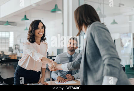 Smiling young businesswoman shaking hands with an office colleague Stock Photo