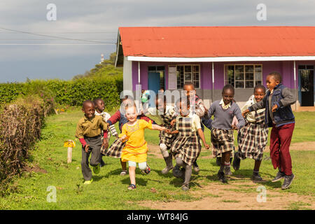 Imani Junior Academy, Nanyuki, Laikipia county, Kenya – June 13th, 2019: Candid photograph of young school children playing with a white girl who was Stock Photo