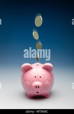 Pink piggy bank with gold coins dropping into it, savings or investment concept Stock Photo