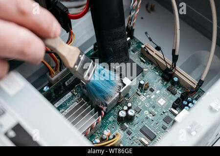 Hand of professional repairman holding a cleaning brush inside old personal computer. PC cleaning and maintenance concept, close up view. Stock Photo