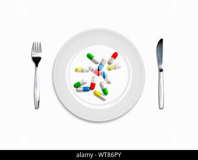 Pills and place setting, white plate, knife and fork with a meal of pill capsules, medicine addiction Stock Photo