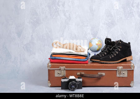 Retro leather suitcase with travel accessories on grey background. Stack of clothes, film photo camera, suede shoes, globe. Travel concept, banner moc Stock Photo
