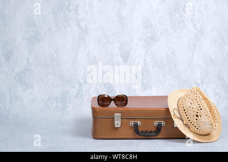 Stylish old fashioned accessories of hipster female traveller: vintage sunglasses, straw hat, leather suitcase on grey background. Concept of travel w Stock Photo