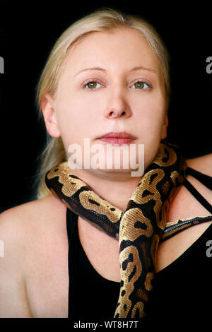 Portrait of girl with Royal Python snake. Woman holds Ball Python snake around neck and in hands, posing in front the camera. Stock Photo
