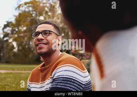 Close-up of a smiling young african man wearing eyeglasses sitting with her girlfriend at park