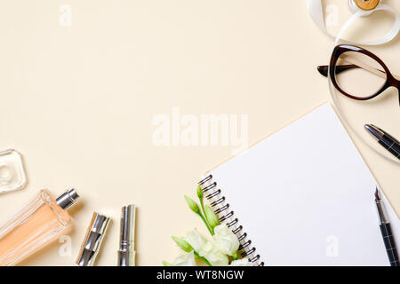 Flat lay feminine accessories, beauty cosmetic, glasses, roses flowers on beige pastel colors background. Top view women desk table with female stuff. Stock Photo