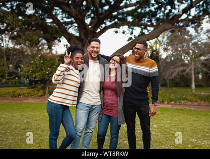 Multiracial group of friends enjoying and standing together in the park looking at camera smiling - very colorful clothing Stock Photo