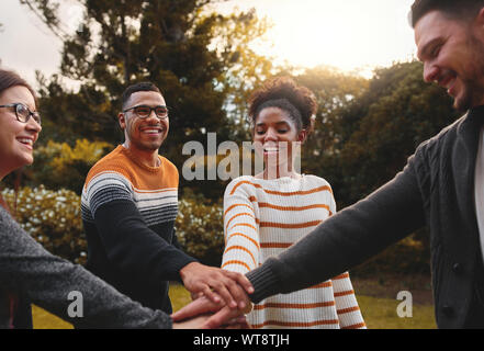Group of smiling diverse friends stacking hands to express unity and support together in park smiling - teamwork  Stock Photo