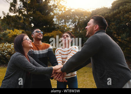 Group of happy multiethnic friends standing together in circle at park stacking their hands Stock Photo