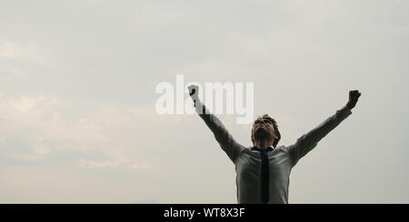Low angle view of young businessman standing with his arms raised under a cloudy sky. Stock Photo