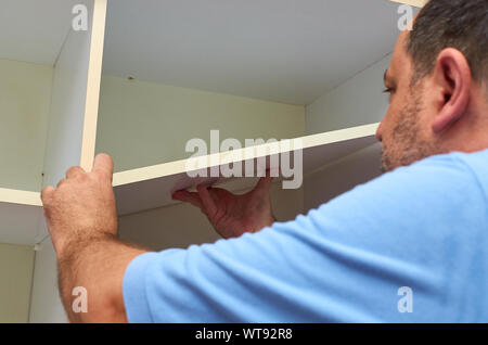 Man installing a shelf in an upper part of a wardrobe Stock Photo