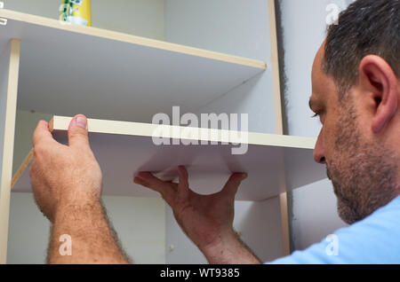 Man installing a shelf in an upper part of a wardrobe Stock Photo