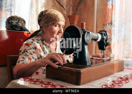 Closeup portrait of old woman using sewing machine, 70 years seamstress working at home Stock Photo