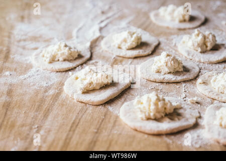 Rolled dough with cottage cheese on wooden table. Process of making homemade dumpling, traditional Russian cuisine Stock Photo