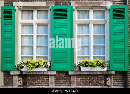 Two retro windows with green wooden shades with yellow flowers on red brick building Stock Photo