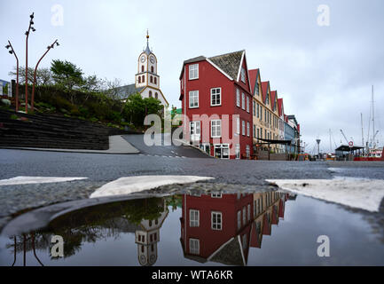 Old town with bright buildings and traditional white church reflected in water of road puddle on Faroe Islands on gloomy day Stock Photo