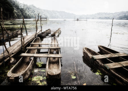 Foggy morning scenic view of traditional fisher boats on Danau Tamblingan lake, popular tourist place in tropical mountain rainforest. Stock Photo