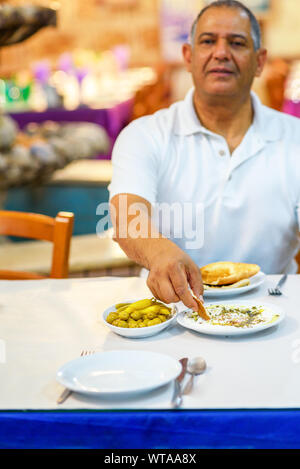 Senior man eat labneh with pita bread. Labneh-soft cheese, similar in texture to cream cheese, made from strained yogurt and very popular in Middle Eastern cuisine. Selective focus on hand and food. Stock Photo