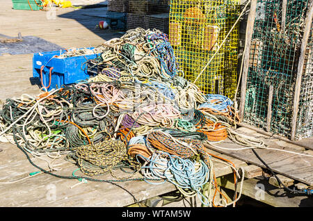 Heap of colourful mooring ropes on a wooden pier in a harbour. Lobster pots are visible in background. Stock Photo
