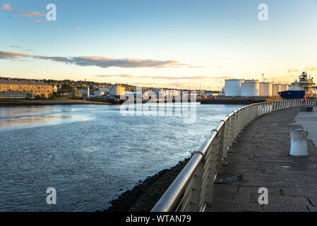 Commercial port with huge fuel tanks as seen from the footpath along the harbour mouth at sunset Stock Photo
