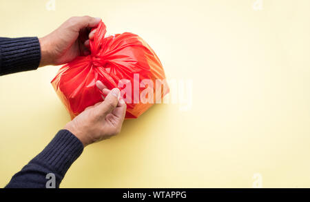Male hand packing food trash with red plastic bag on color background.Recycle and environment concepts ideas Stock Photo
