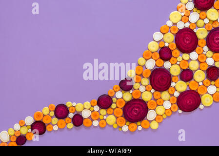 Slices of vegetable roots isolated on a purple background. Above view of cold season vegetables. Winter vegetable pattern. Colorful raw winter food. Stock Photo