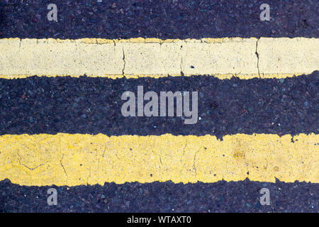 Two parallel yellow road marking lines running horizontally on black tarmac Stock Photo